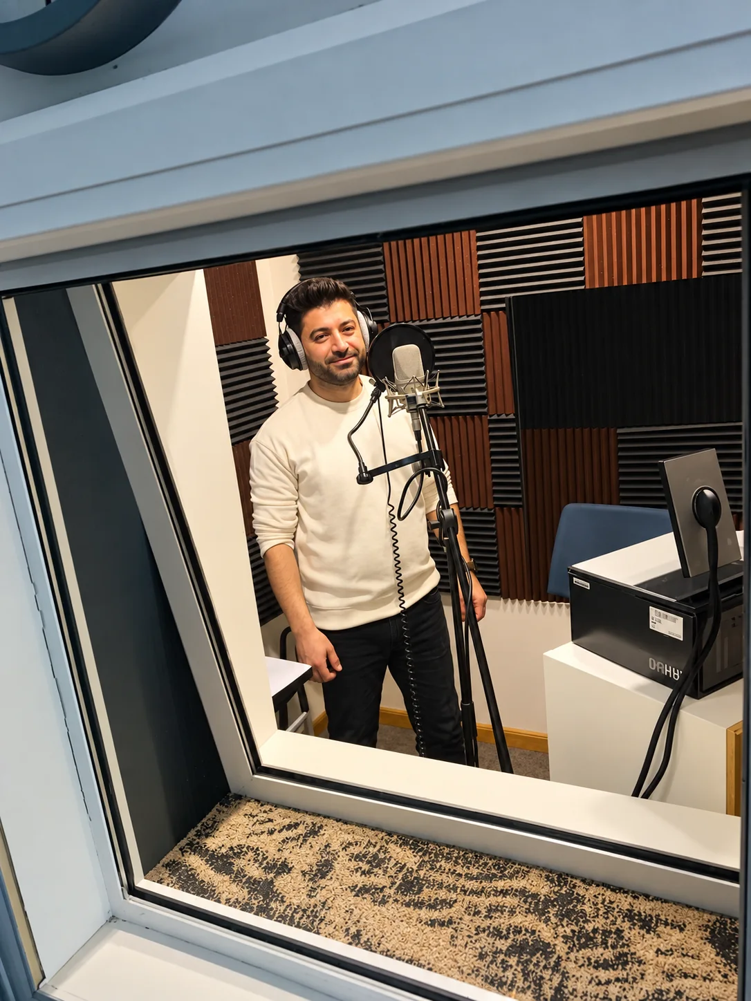 TABADUL voice talent recording behind the booth glass, headphones on, mic in shot